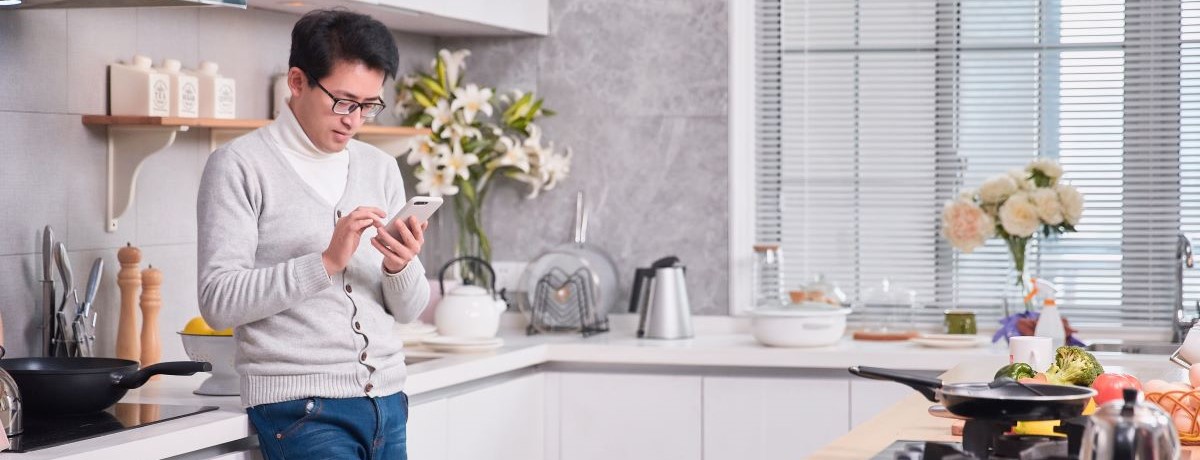 man preparing food and texting in kitchen 